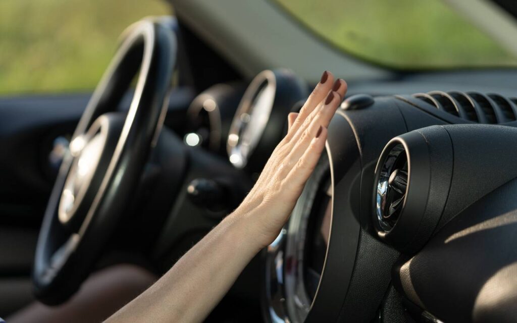 Donna che mette la mano davanti alla bocchetta dell'aria condizionata in auto