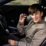 ragazzino dentro un'auto dalla parte del conducente che mostra le chiavi dell'auto