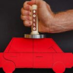 Illustrazione di un batti carne con scritto "bollo" che schiaccia un'auto di carta