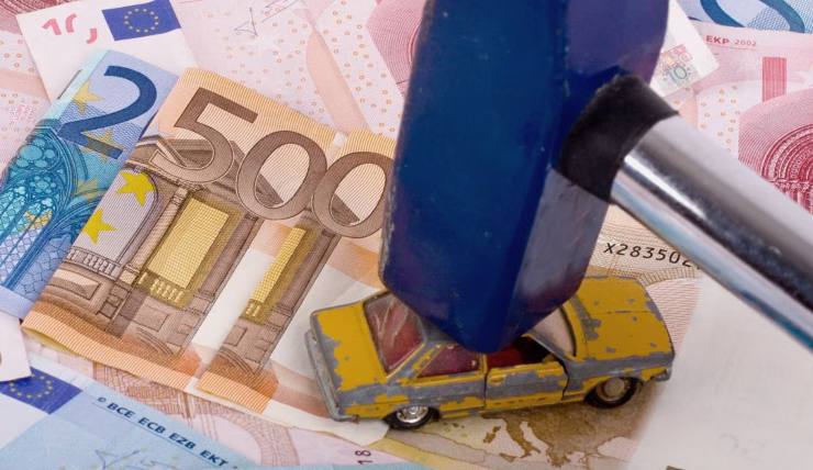 Martello che schiaccia un vecchio modellino d'auto sopra a banconote euro