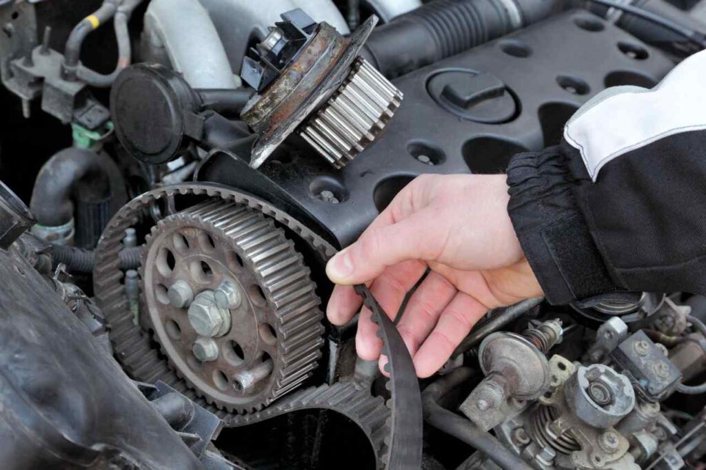 meccanico che tocca la cinghia di distribuzione di un'auto