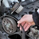 meccanico che tocca la cinghia di distribuzione di un'auto