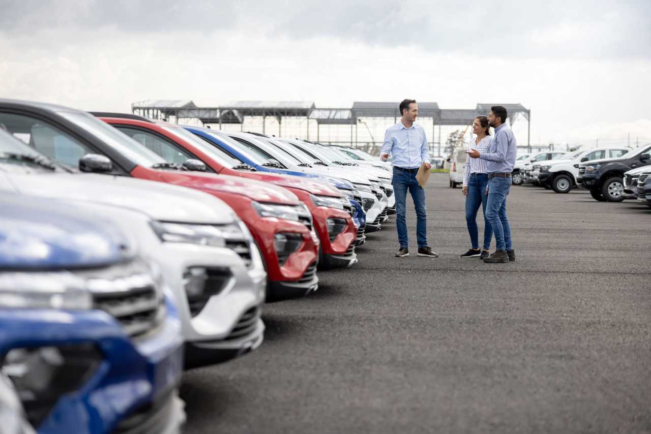 Concessionaria auto all'aperto con commerciante e una coppia di clienti