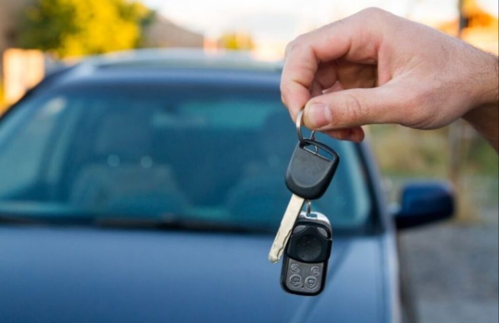 Auto sullo sfondo e mano di un uomo che mostra le chiavi dell'auto in primo piano