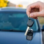 Auto sullo sfondo e mano di un uomo che mostra le chiavi dell'auto in primo piano