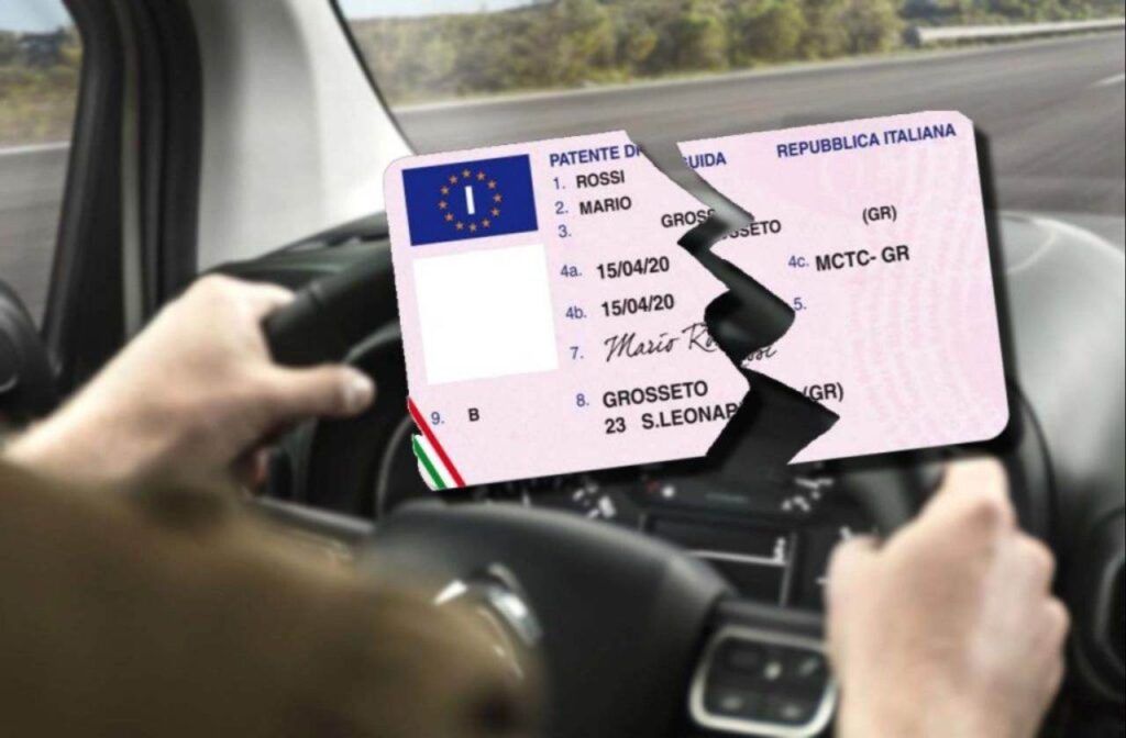 Persona alla guida sullo sfondo e patente rotta in due in primo piano