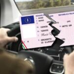 Persona alla guida sullo sfondo e patente rotta in due in primo piano