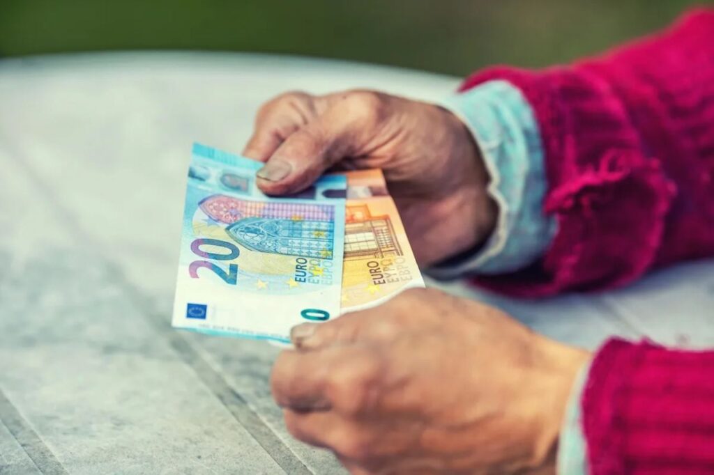Mano di un anziano che tiene due banconote da 20 e 50€