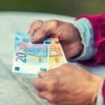 Mano di un anziano che tiene due banconote da 20 e 50€