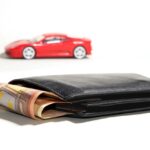 Portafoglio pieno in primo piano e modellino d'auto sullo sfondo