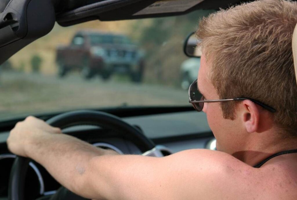 Uomo che guida a torso nudo la sua auto
