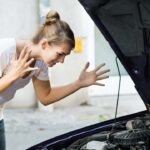 Ragazza che guarda dentro al cofano perché l'auto non parte