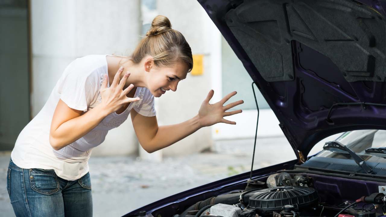 Ragazza che guarda dentro al cofano perché l'auto non parte