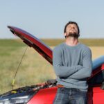 Uomo disperato appoggiato sulla sua auto rotta e cofano alzato