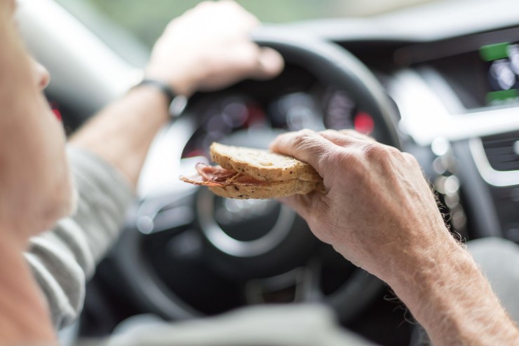 Uomo che mangia un tramezzino alla guida dell'auto