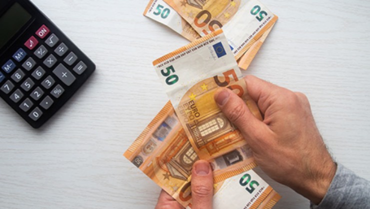 Uomo con in mano diverse banconote da 50€ e calcolatrice vicina
