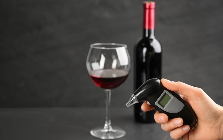 alcol test in mano, bottiglia e bicchiere di vino sullo sfondo