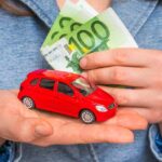 Persona con modellino auto in mano e banconote da 100€