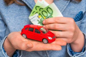 Persona con modellino auto in mano e banconote da 100€
