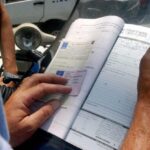 Vigile che fa una multa con patente e libretto di un conducente in mano