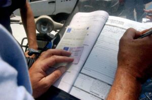 Vigile che fa una multa con patente e libretto di un conducente in mano