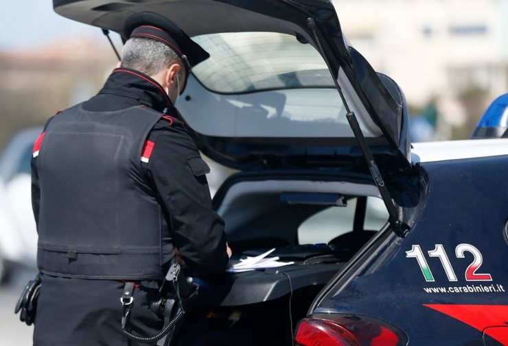 Carabiniere di schiena che compila una sanzione appoggiato all'auto