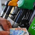 Pompa di benzina e mano di un uomo che tiene delle banconote