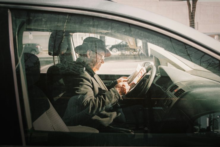 Anziano in auto dal lato conducente che legge un giornale