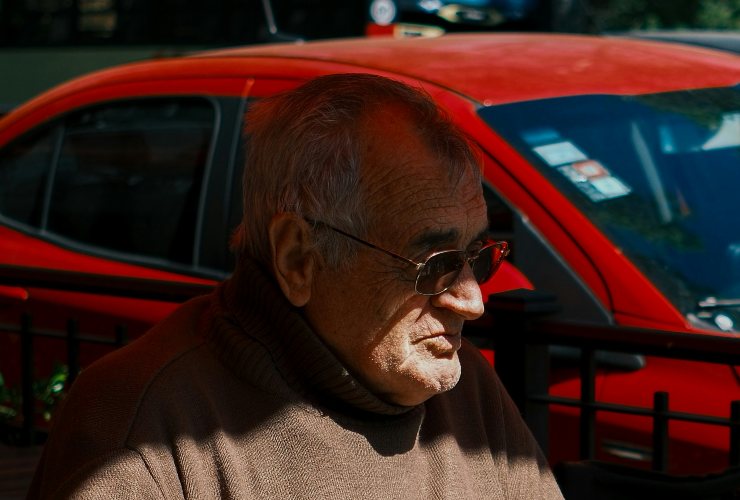 Anziano primo piano e auto rossa sullo sfondo