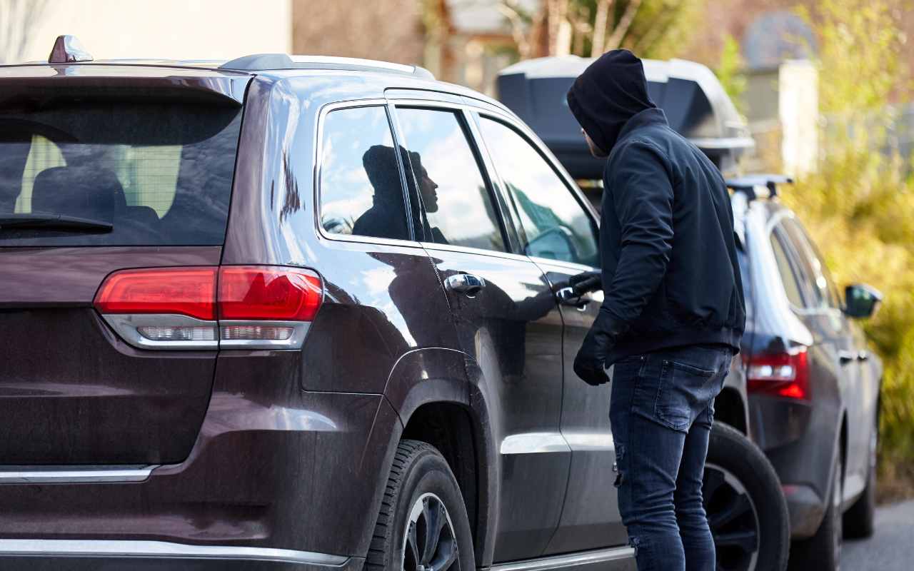 Uomo incappucciato che apre un'auto per rubarla