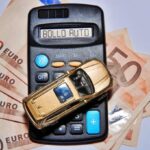 Una macchina giocattolo sopra a una calcolatrice con critto bollo auto, a sua volta sopra a banconote da 50€
