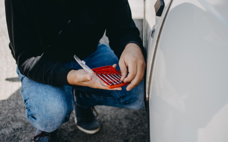 Uomo chinato mentre cerca il cacciavite giusto per scassinare un'auto
