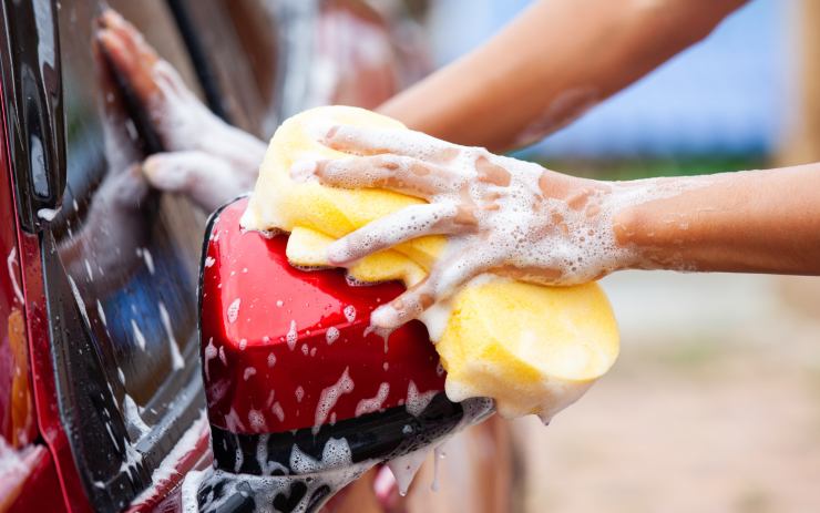 Persona che lava lo specchietto dell'auto con una spugna piena di schiuma
