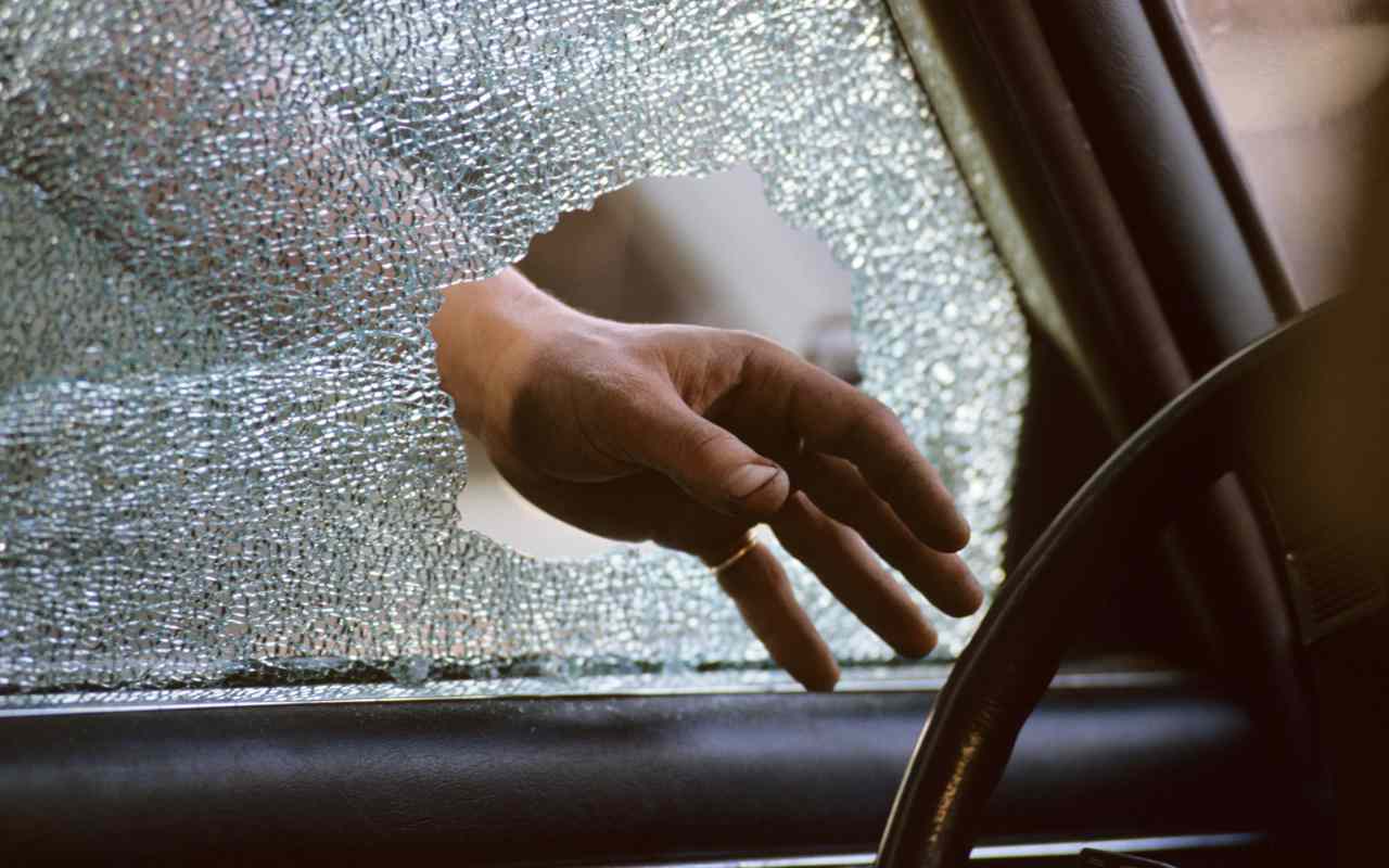 Ladro che infila la mano dentro un finestrino rotto di un'auto
