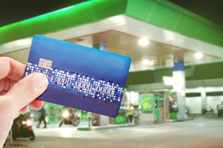 benzinaio sullo sfondo e carta di credito in mano in primo piano