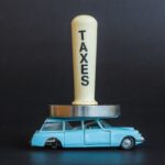 Batti carne con la scritta "Taxes" che schiaccia un'auto