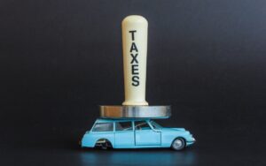 Batti carne con la scritta "Taxes" che schiaccia un'auto